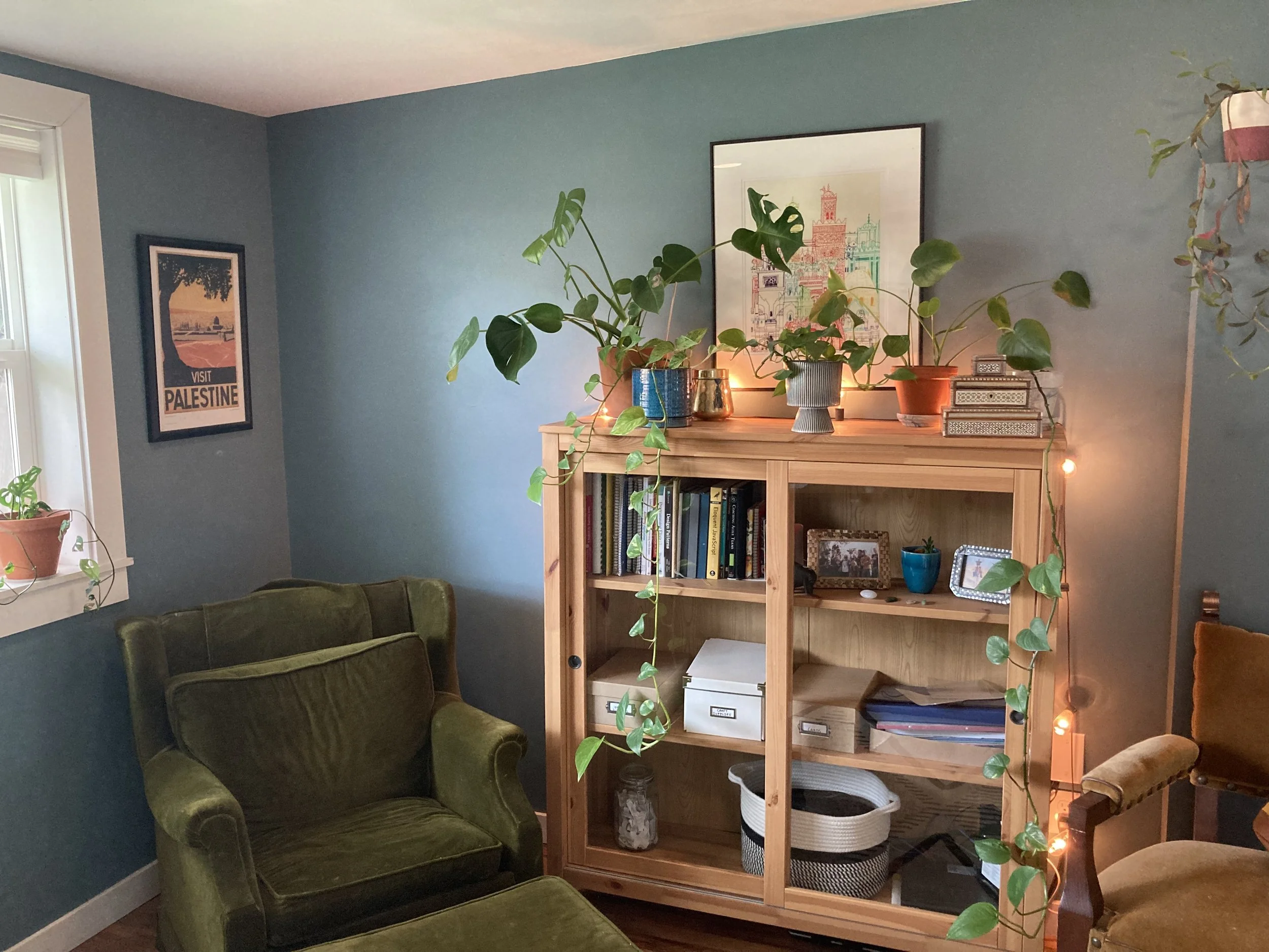 Bookshelf with plants with forest green chair on the left in a room with blue grey walls.