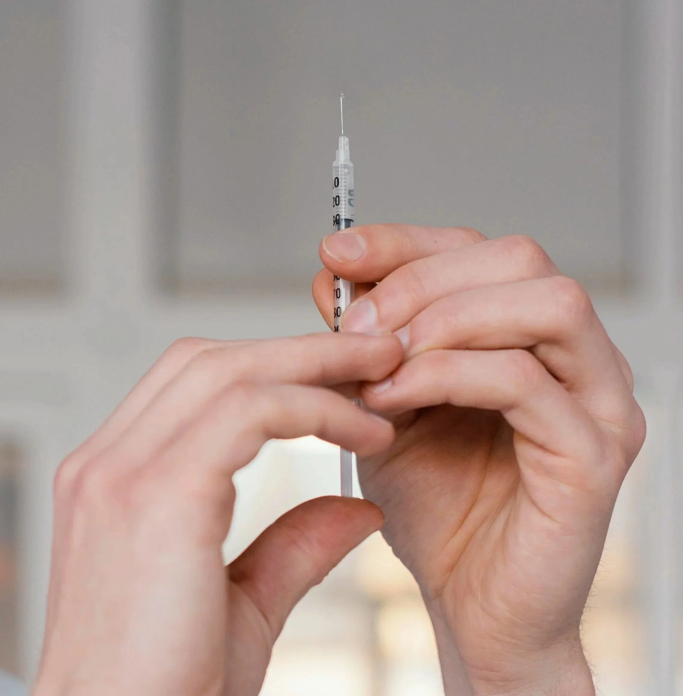 Person holding a syringe with a needle, preparing for an injection in a home setting.