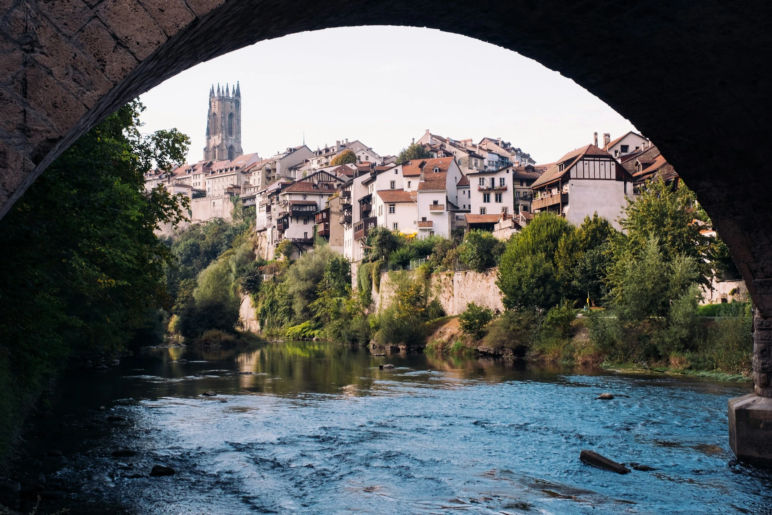 Blick durch eine Brücke auf eine Stadt auf einem Hügel mit Fluss im Vordergrund, mittelalterliche Architektur und Kirchturm