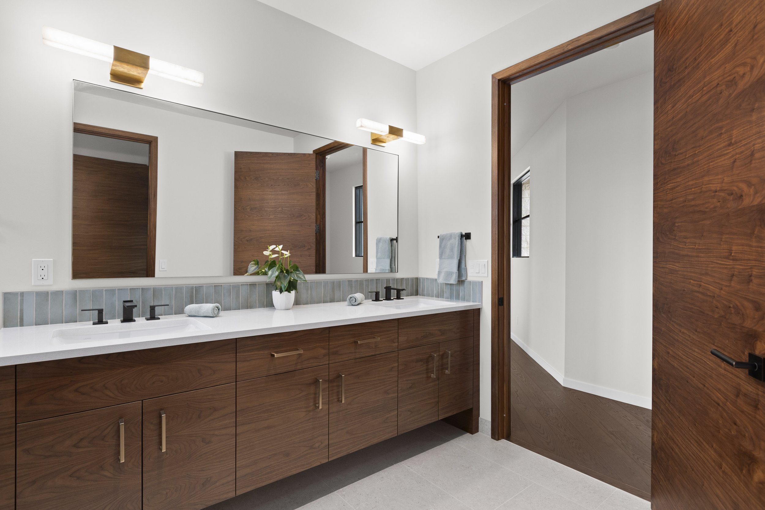 Secondary bathroom vanity detail with walnut cabinetry and tile backsplash