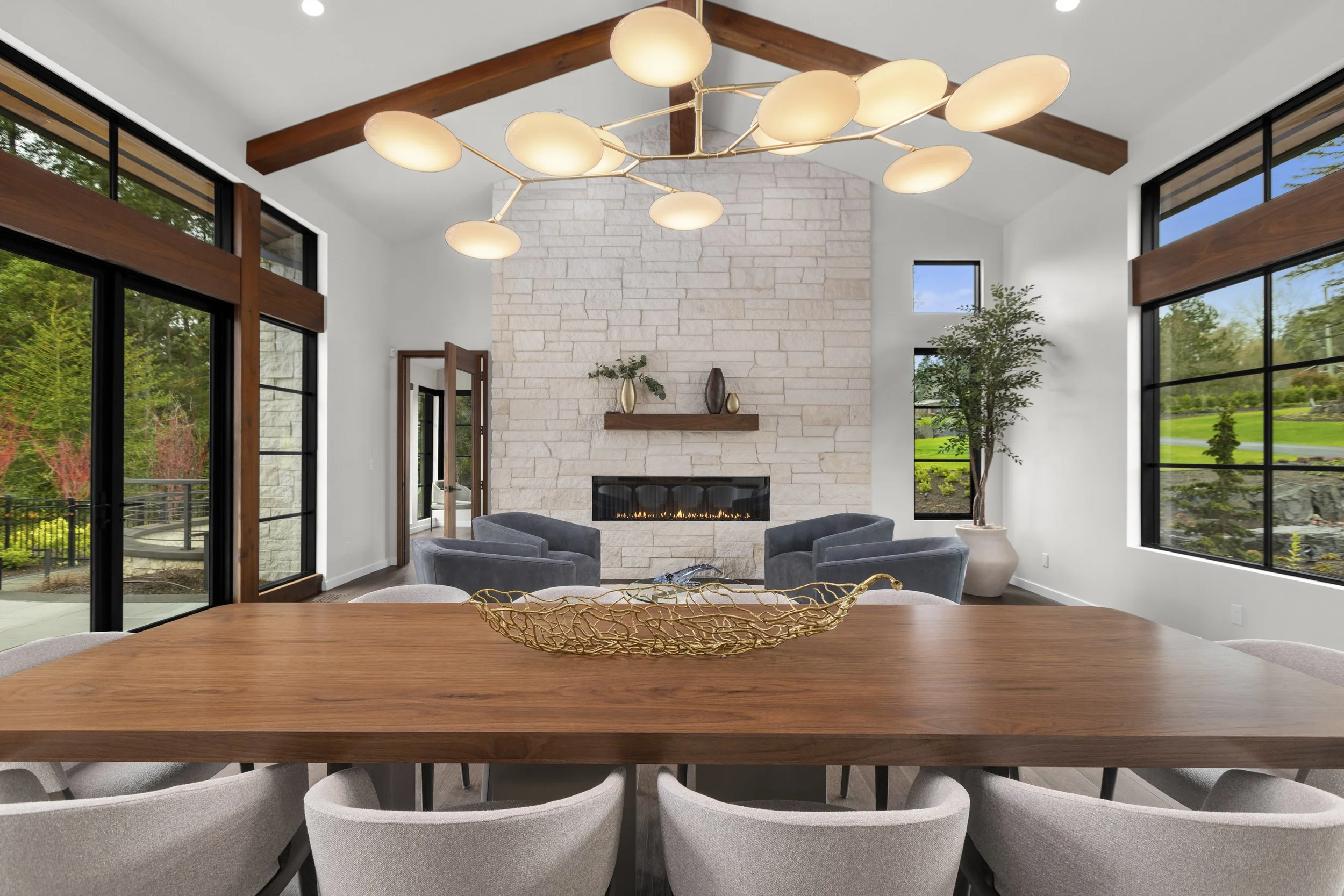 Custom walnut dining table in a modern Pacific Northwest home with exposed wood beams, floor-to-ceiling windows, stone fireplace, and built-in millwork by Madera Furniture Company.
