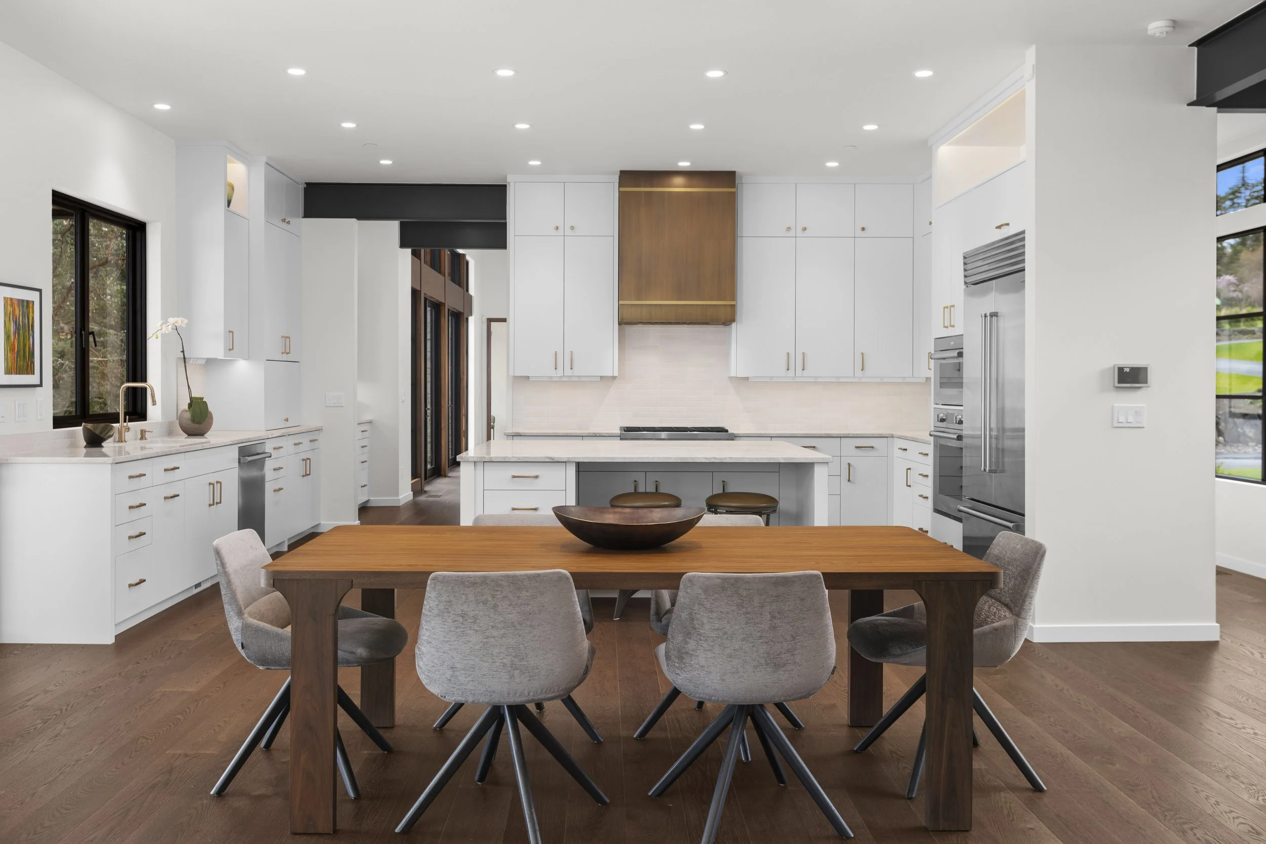 Modern kitchen with wooden cabinets and a large wooden kitchen island, pendant lights, and a view of an outdoor balcony with trees in the background.
