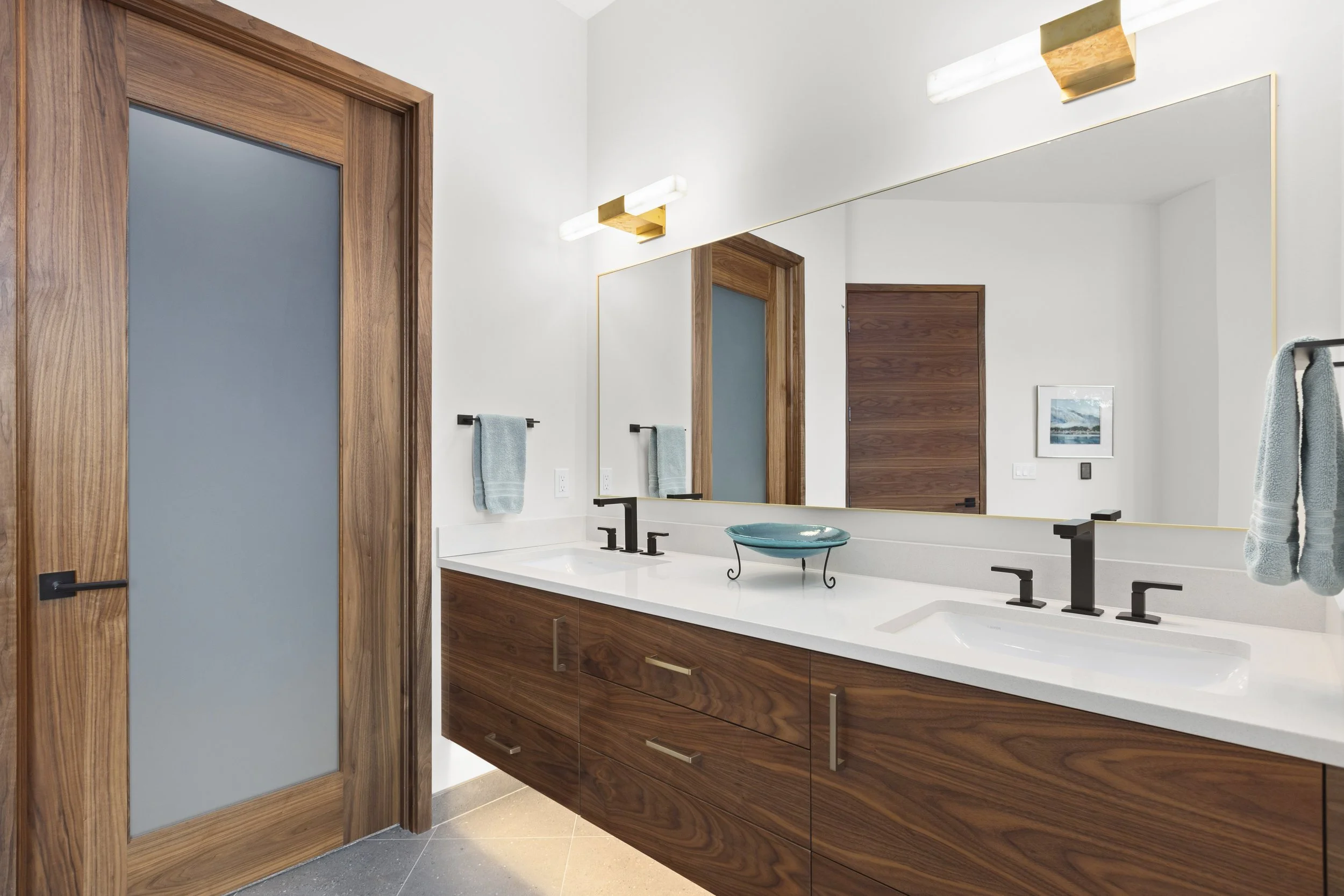 Primary bath vanity detail with custom walnut cabinetry and integrated lighting mirrors