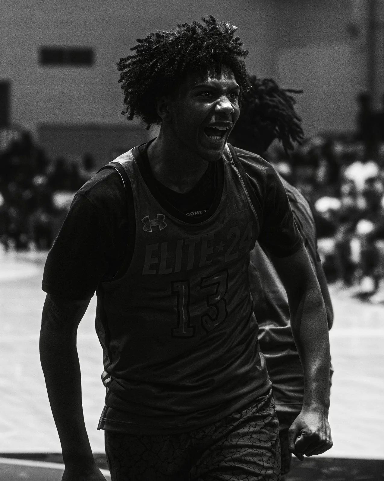 A Black male basketball player with dreadlocks, wearing a jersey with the number 15, appears excited or celebrating during a game.