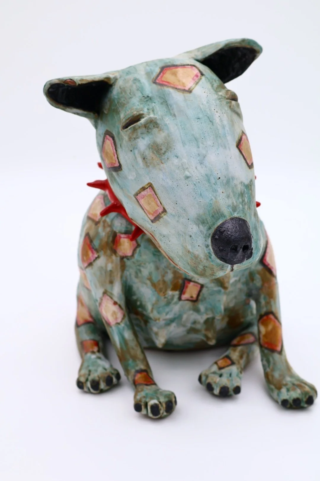 A decorative sculpture of a dog with a long snout, painted with geometric patterns and a weathered distressed finish.
