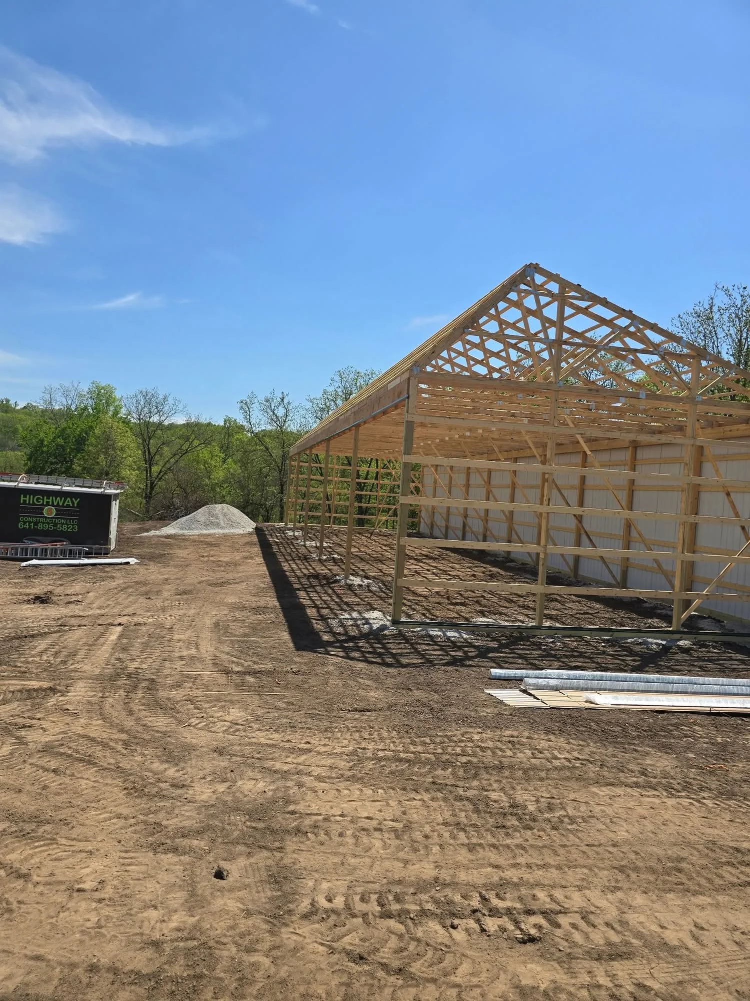 Construction site with a wooden frame structure under a clear blue sky, surrounded by dirt and some construction equipment.