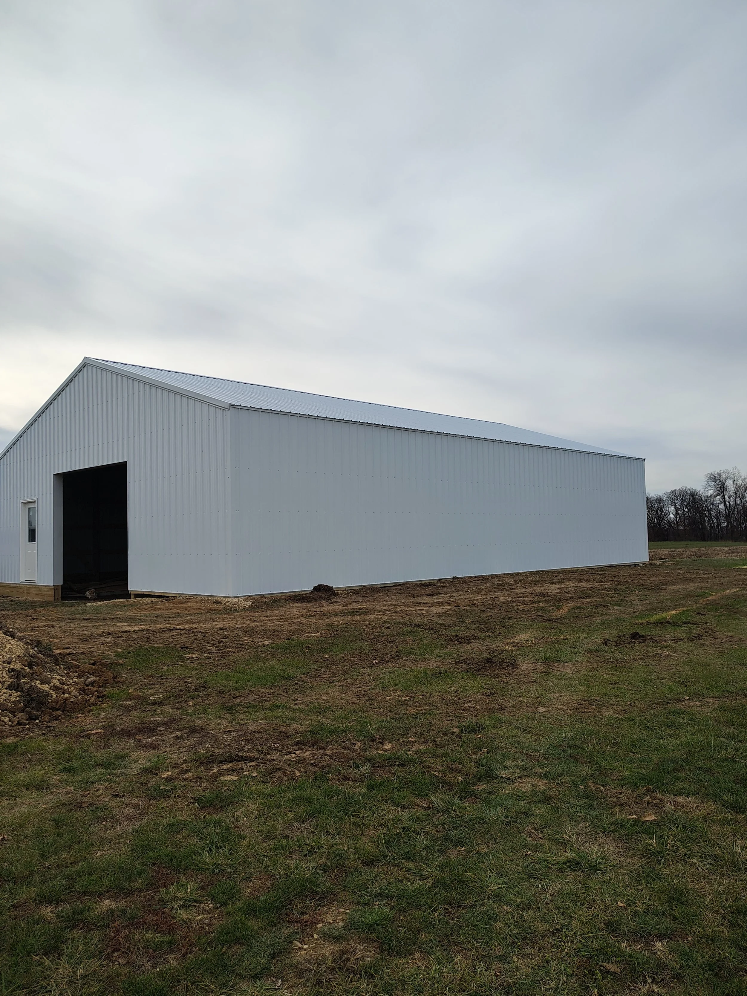A large white metal barn on a grassy field with a cloudy sky overhead.