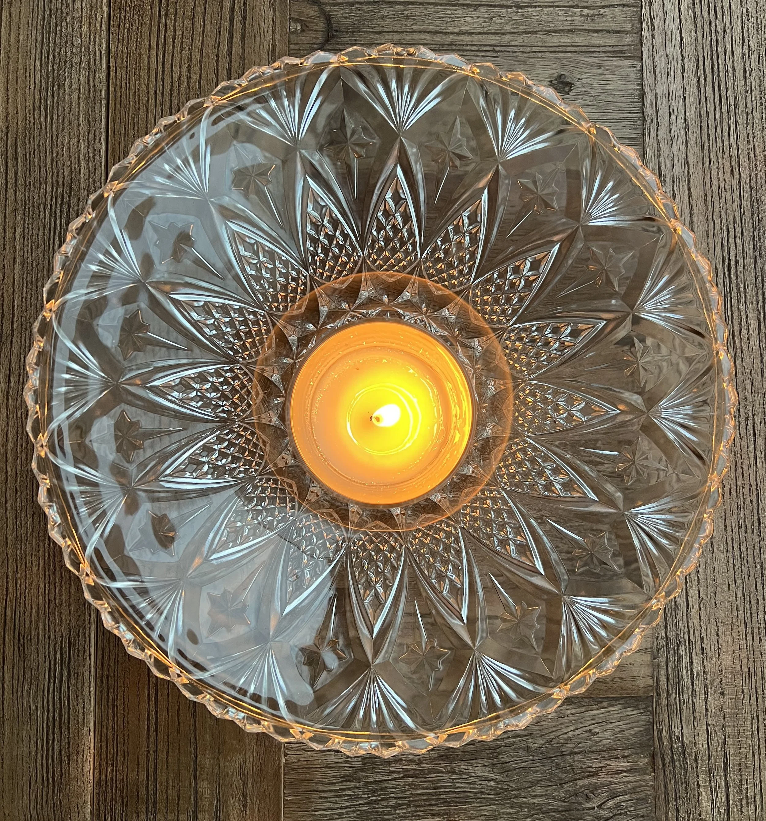 A decorative glass holder with a lit candle inside, placed on a dark wooden surface.