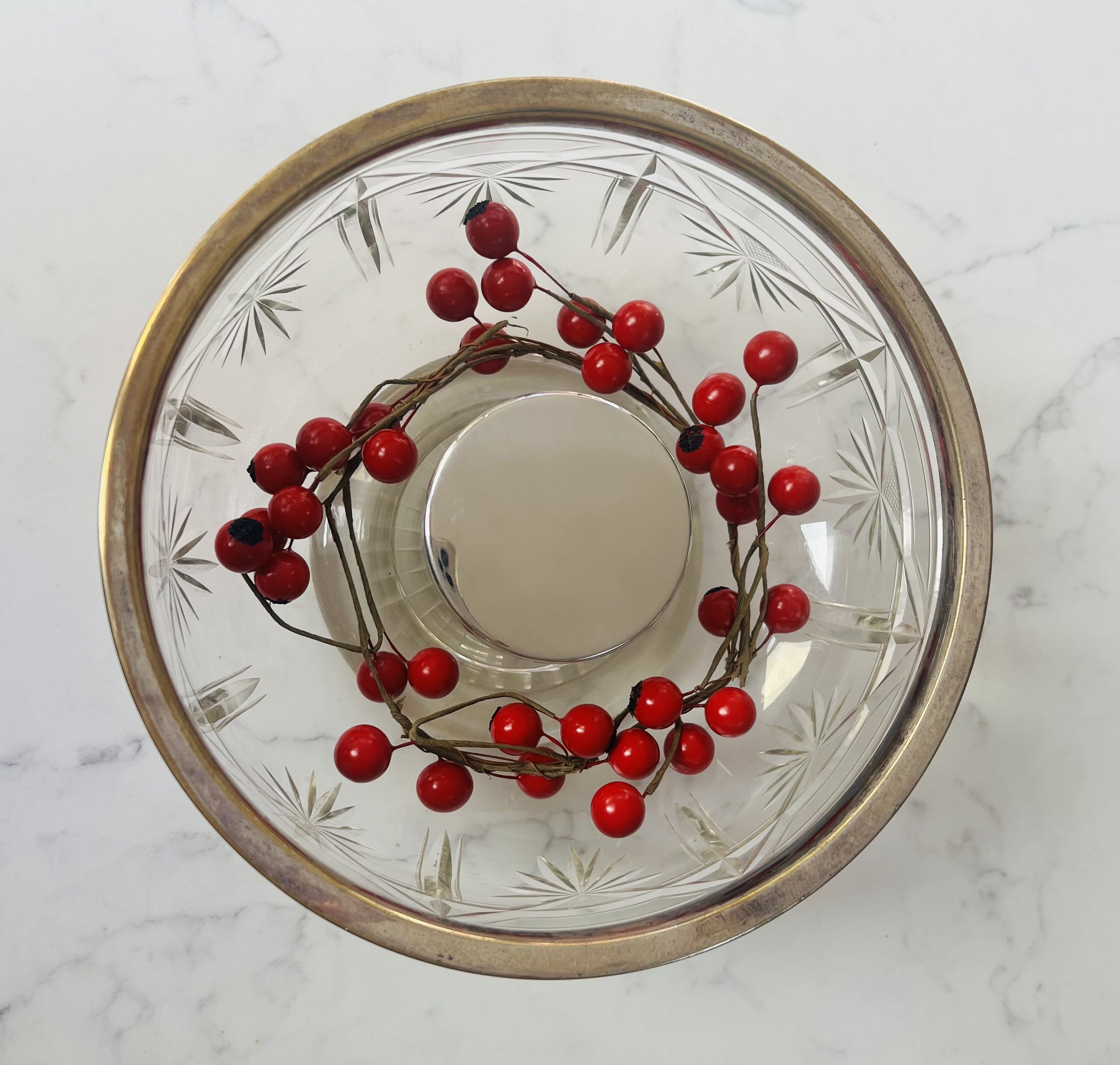 Top view of a round, clear glass bowl with gold rim and etched starburst pattern, containing a wreath of red berries.