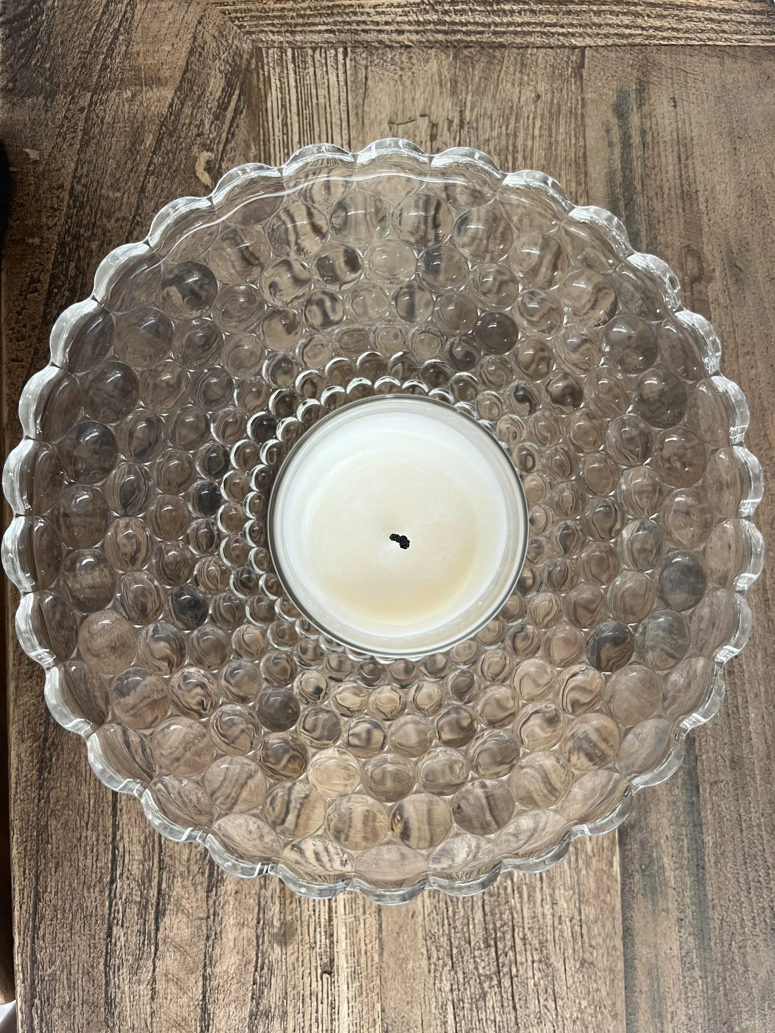 A decorative glass bowl with a scalloped edge and a textured, bubble-like pattern, holding a white candle in the center.