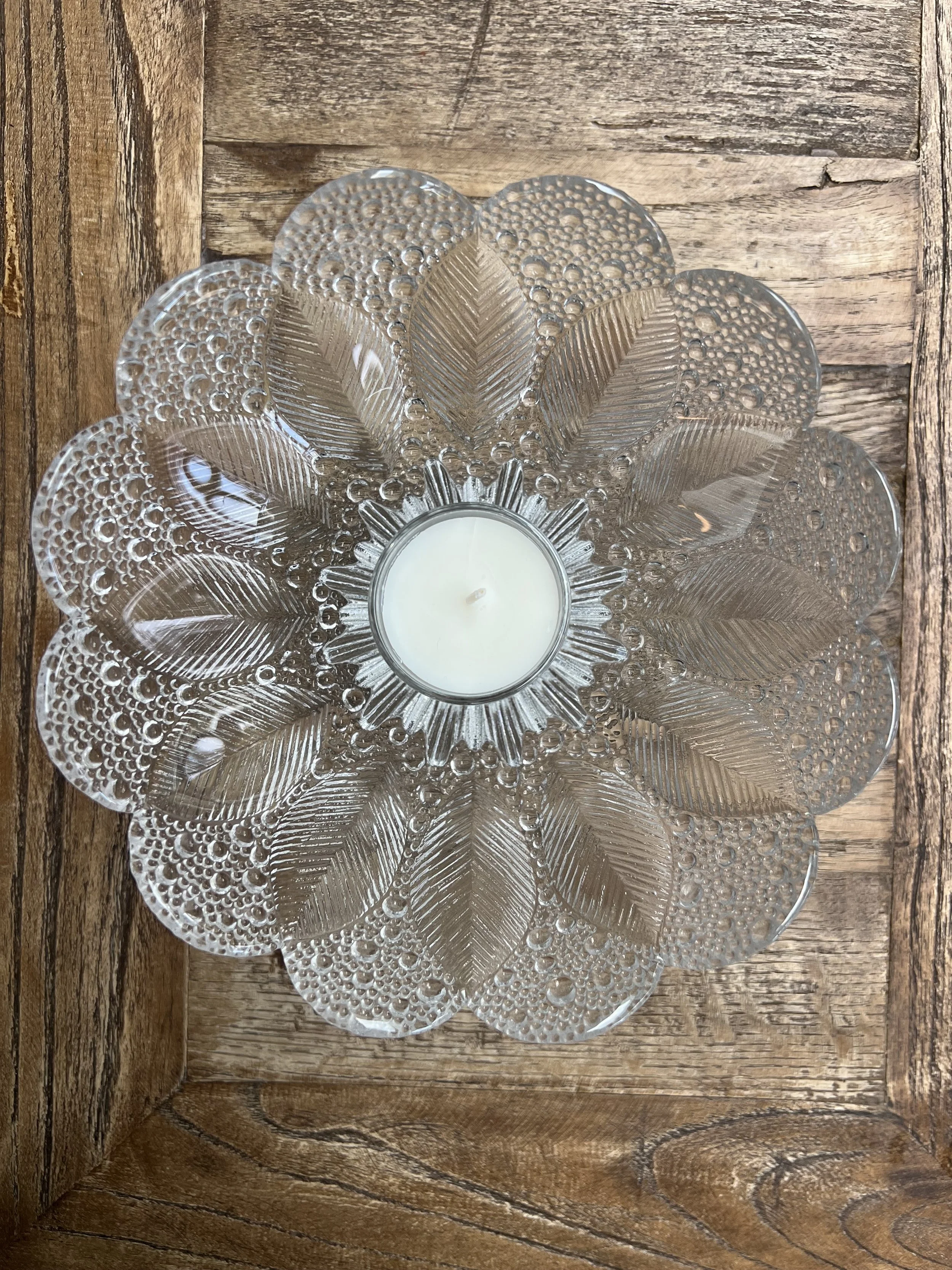 Decorative glass candle holder shaped like a flower with a white candle inside, placed on a wooden surface.