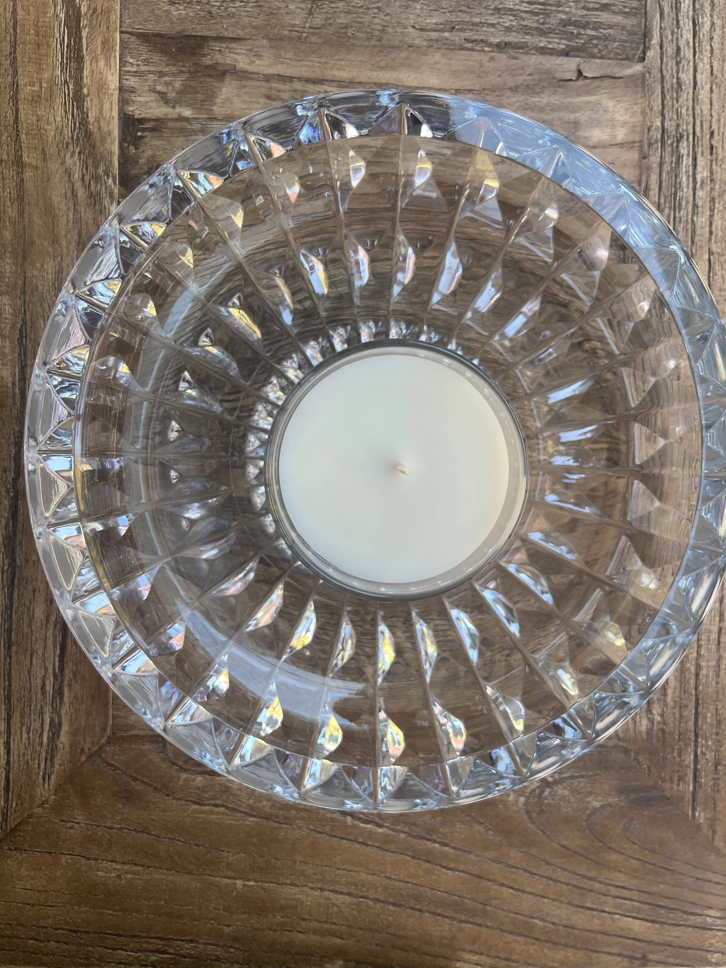 A white candle in a clear, faceted glass candle holder on a wooden surface.