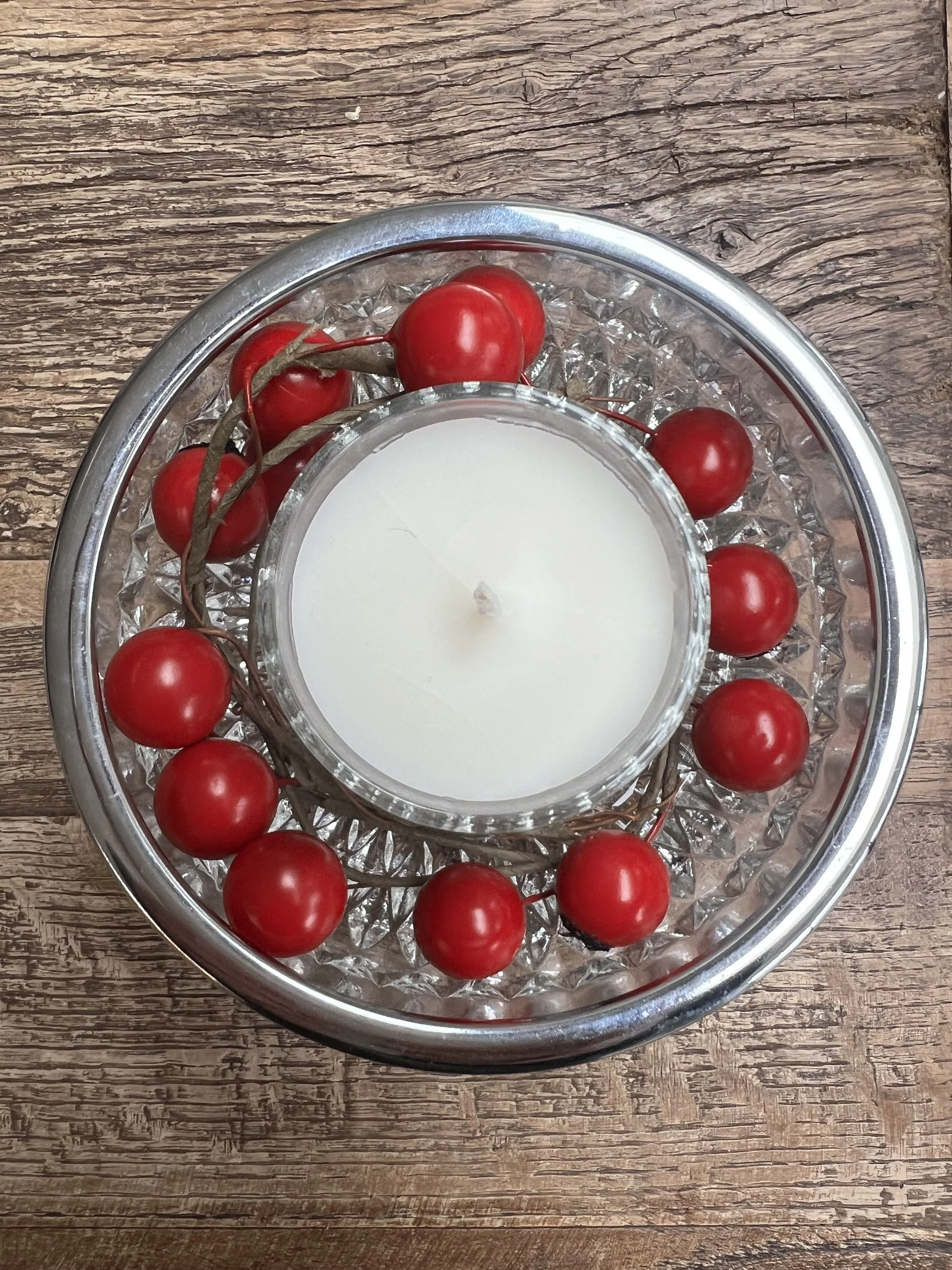 A decorative glass candle holder with red berries around it, placed on a wooden surface.
