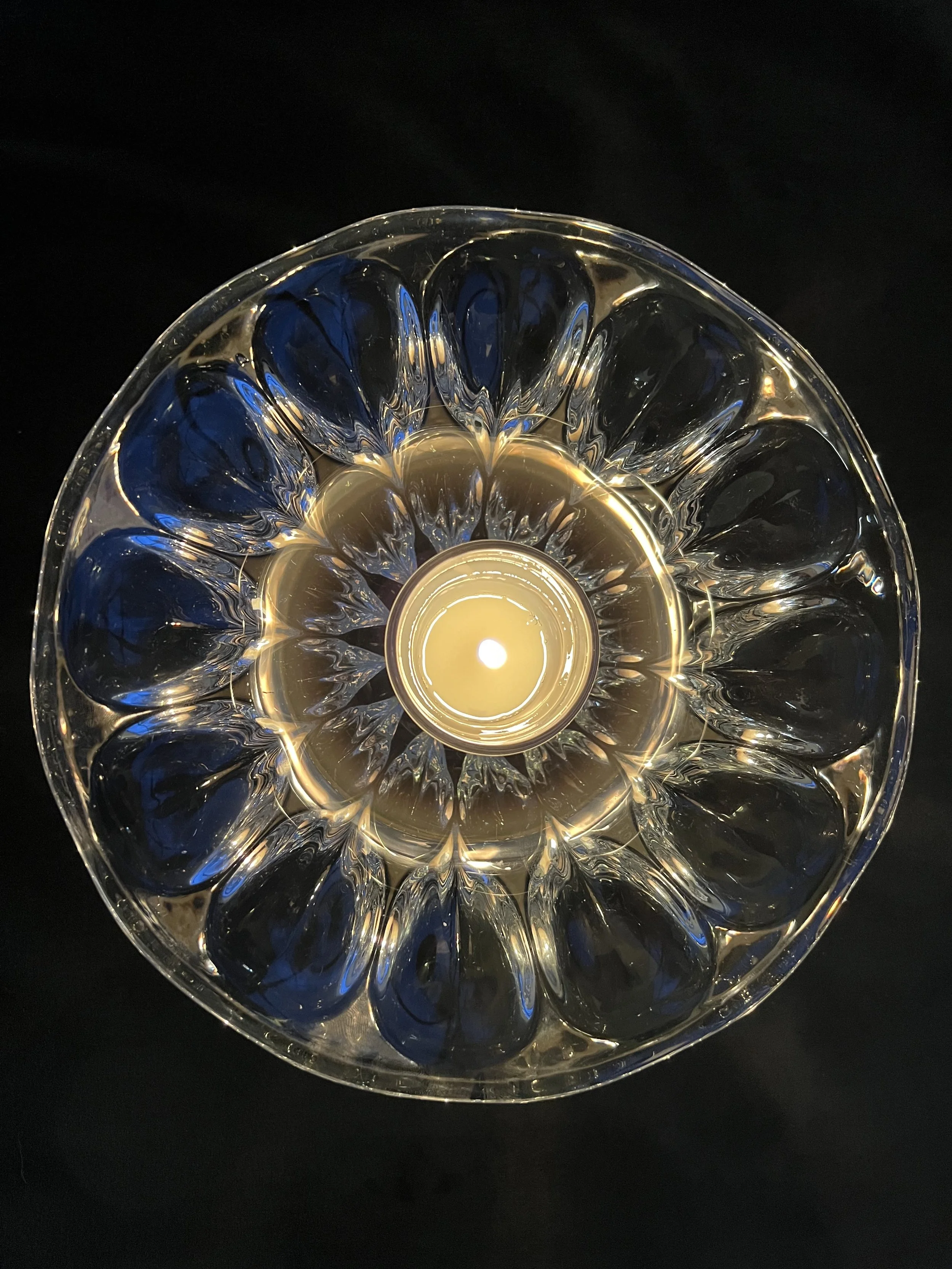 Top view of a decorative glass bowl with intricate patterns, illuminated from within against a dark background.