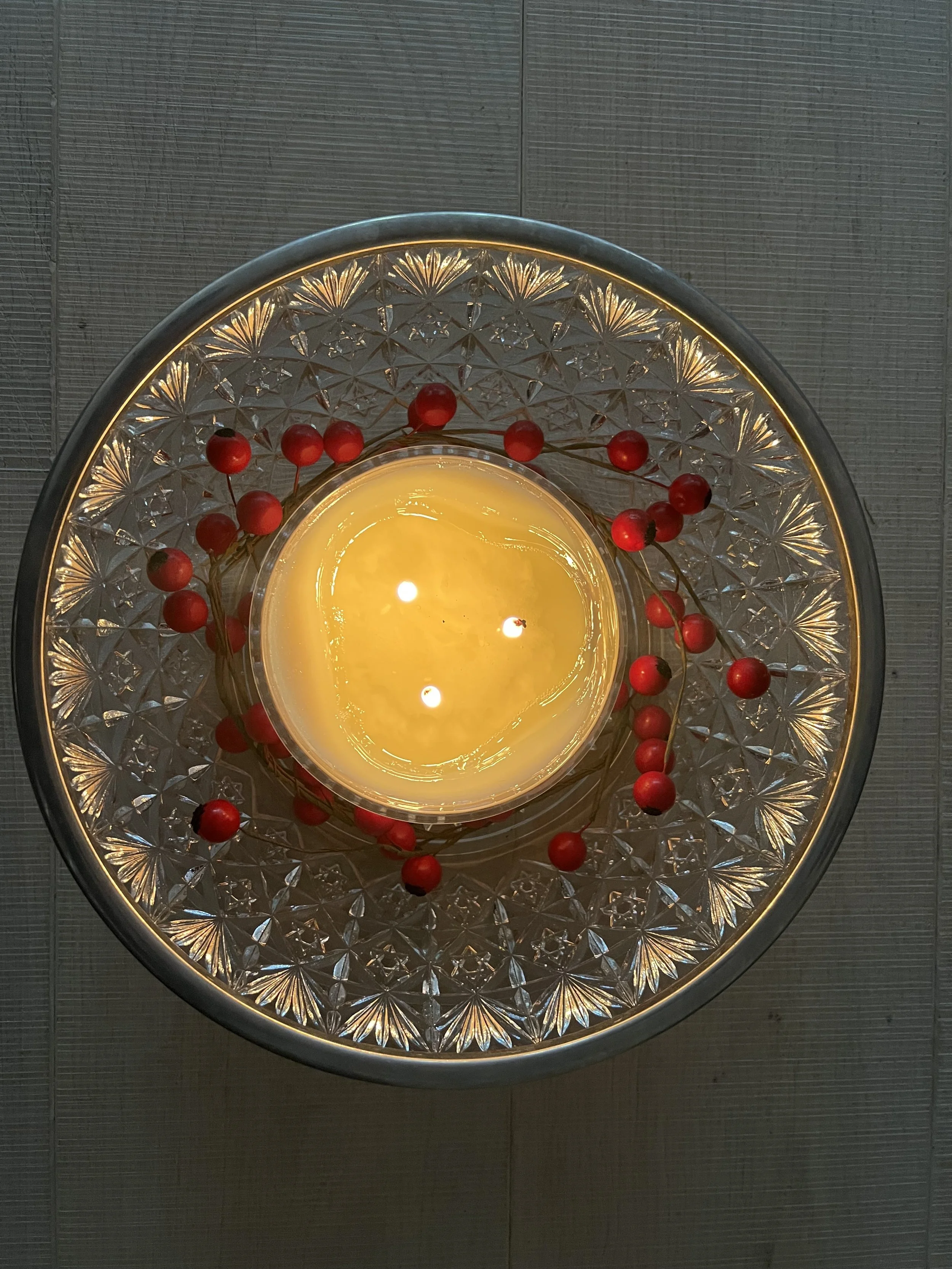 Framed candle on a glass tray decorated with red berries.