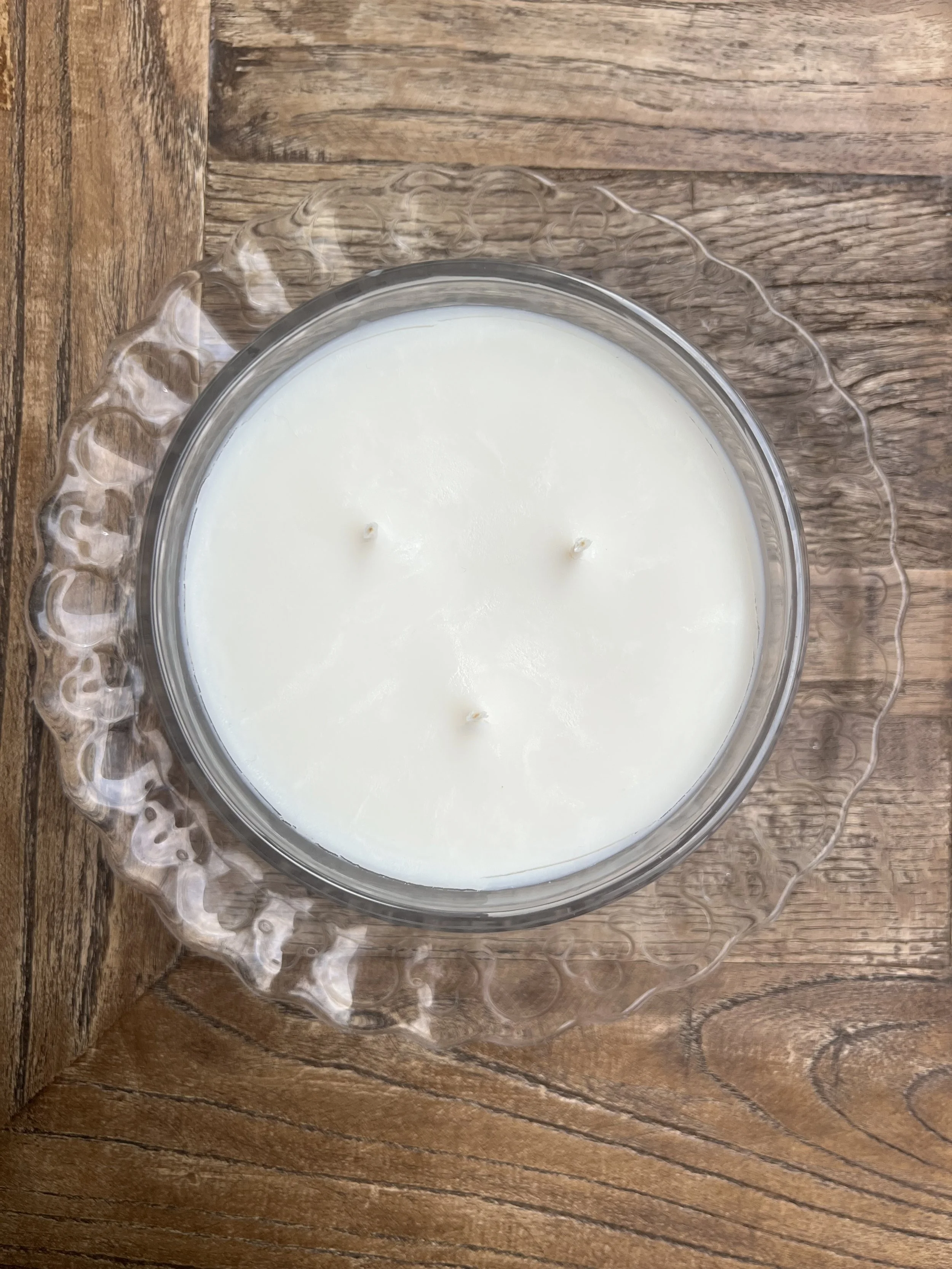 White candle with three wicks in a glass holder placed on a wooden surface.