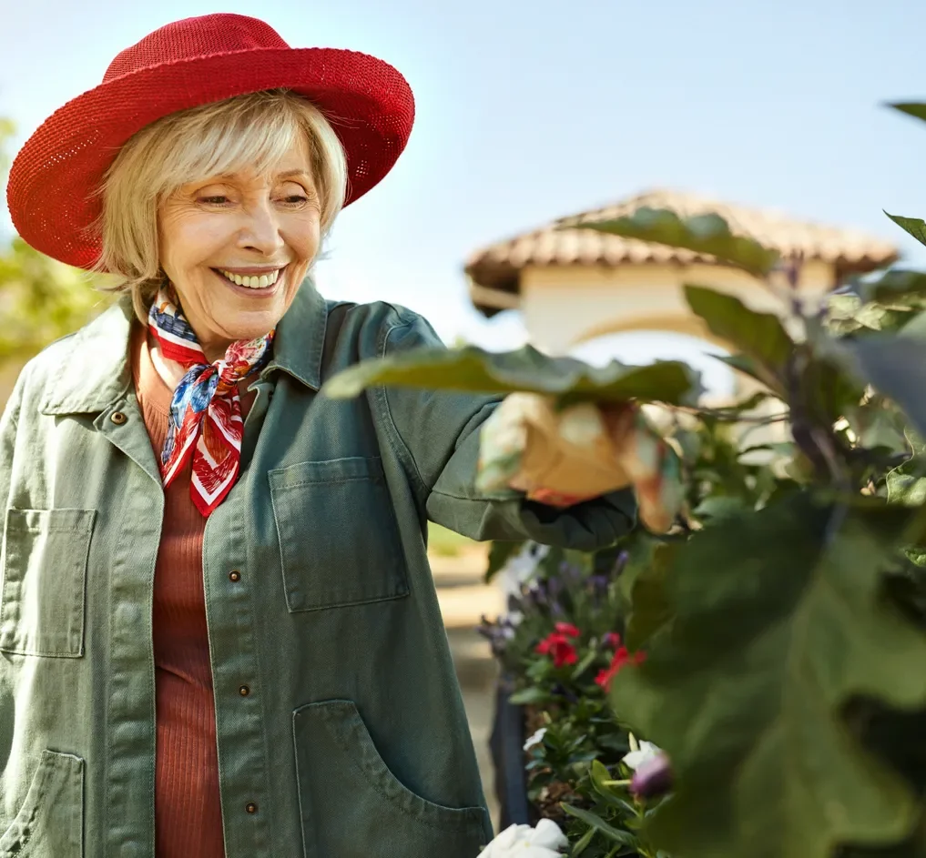 A happy senior lady in a red hat tending to a garden