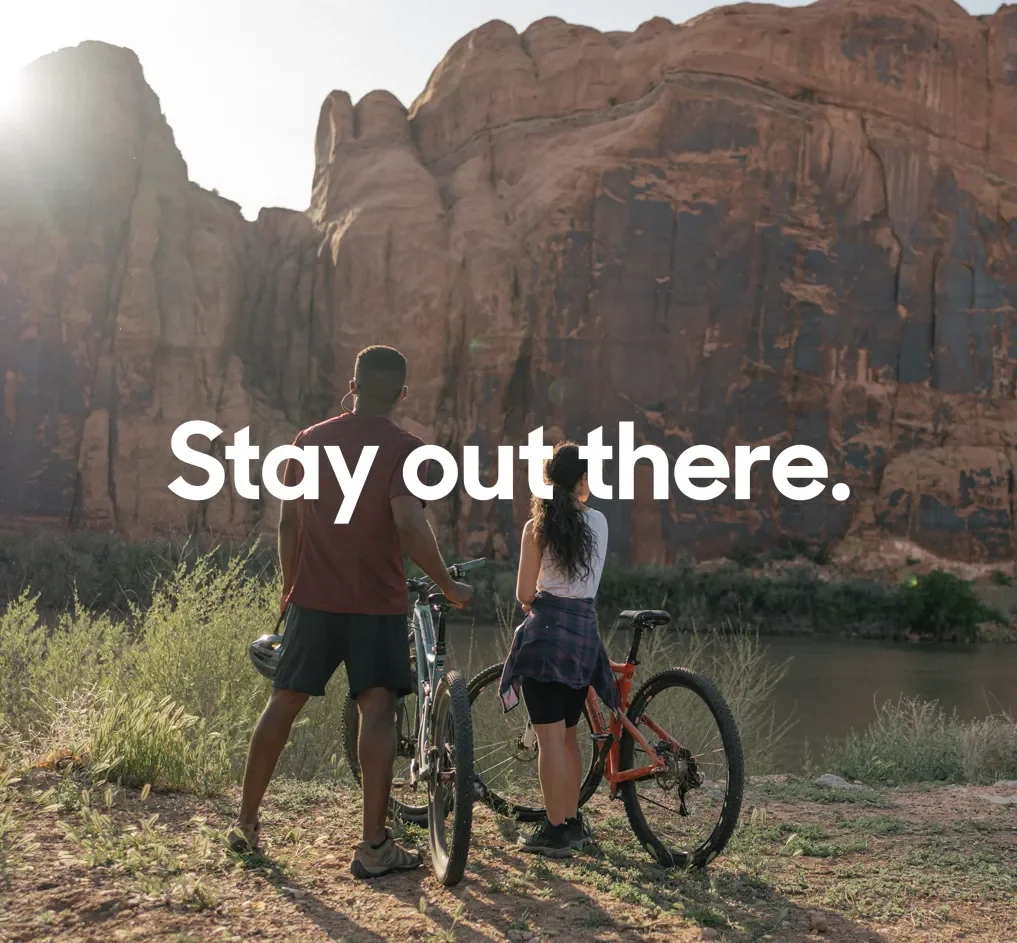 A man and a woman taking a break on the mountain bikes gazing at the Moab nature with the words Stay out there