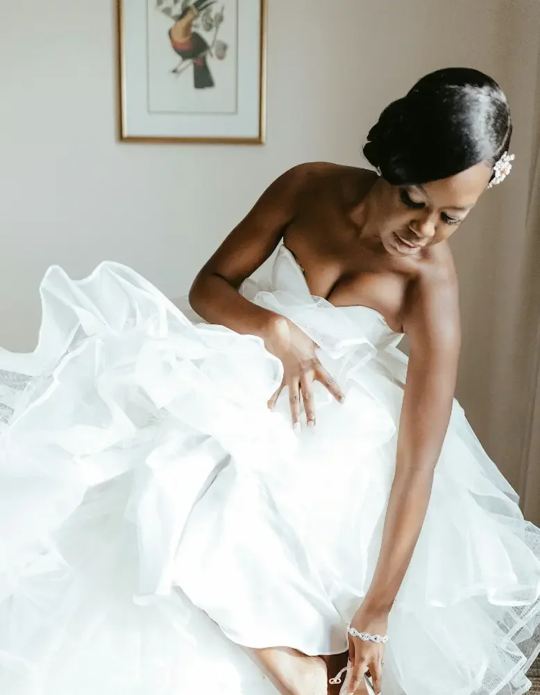 Bride wearing a tulle layered dress with floral haircomb, diamond bracelet  looking at her shoes.