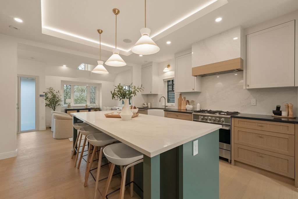 Modern kitchen with white and wood cabinets, a large island with seating, pendant lighting, and a living area in the background.