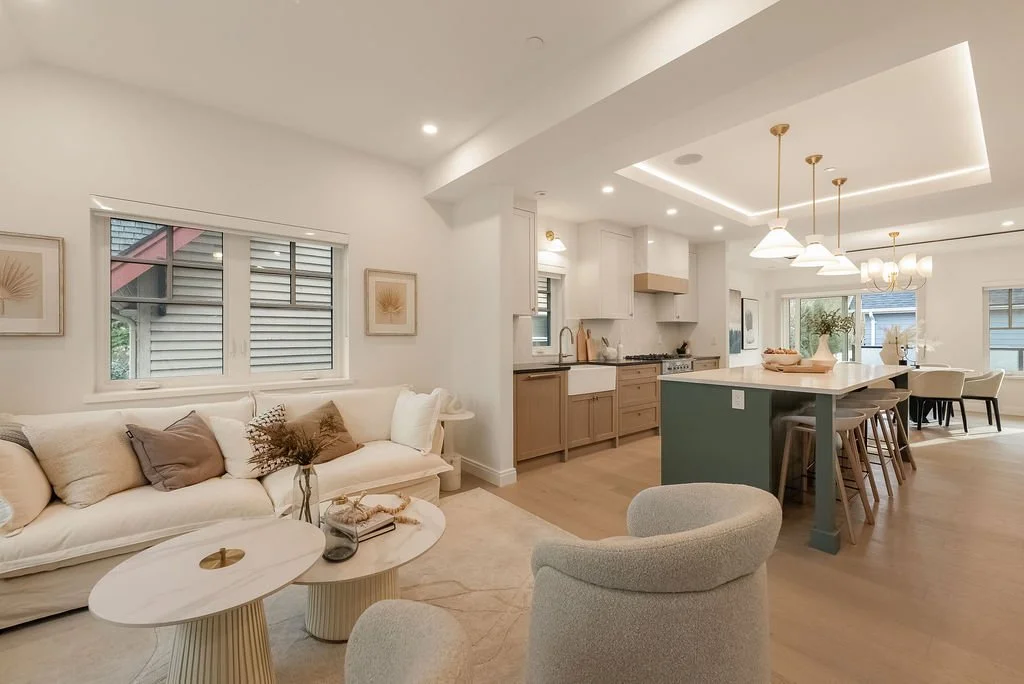 Open-concept living room and kitchen with modern decor, white walls, large windows, and a kitchen island with barstools.