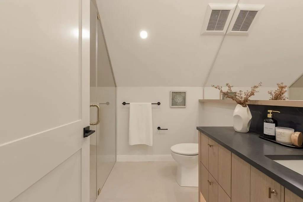 Modern bathroom with a walk-in shower, toilet, wooden vanity, and decorative vase with dried branches.