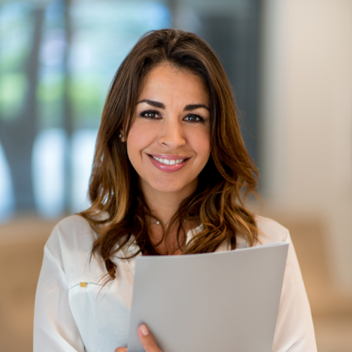 A smiling woman holding a gray folder in an office setting.