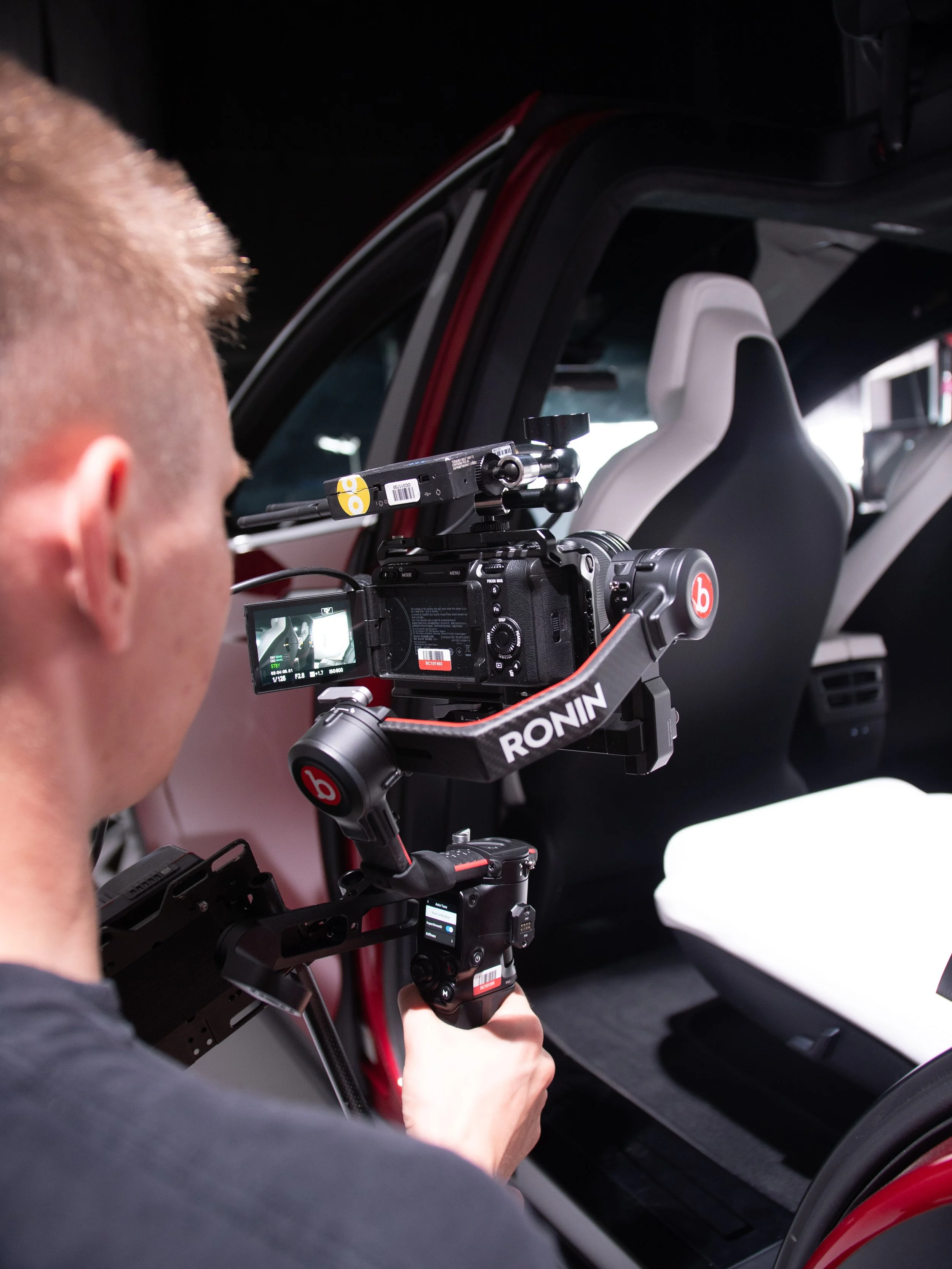 A person operating a camera mounted on a stabilizer rig inside a vehicle, taking photos or videos of the car interior.