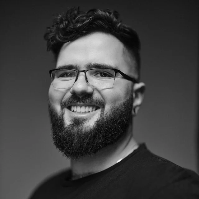 Black and white portrait of smiling man with glasses, beard, and short curly hair.