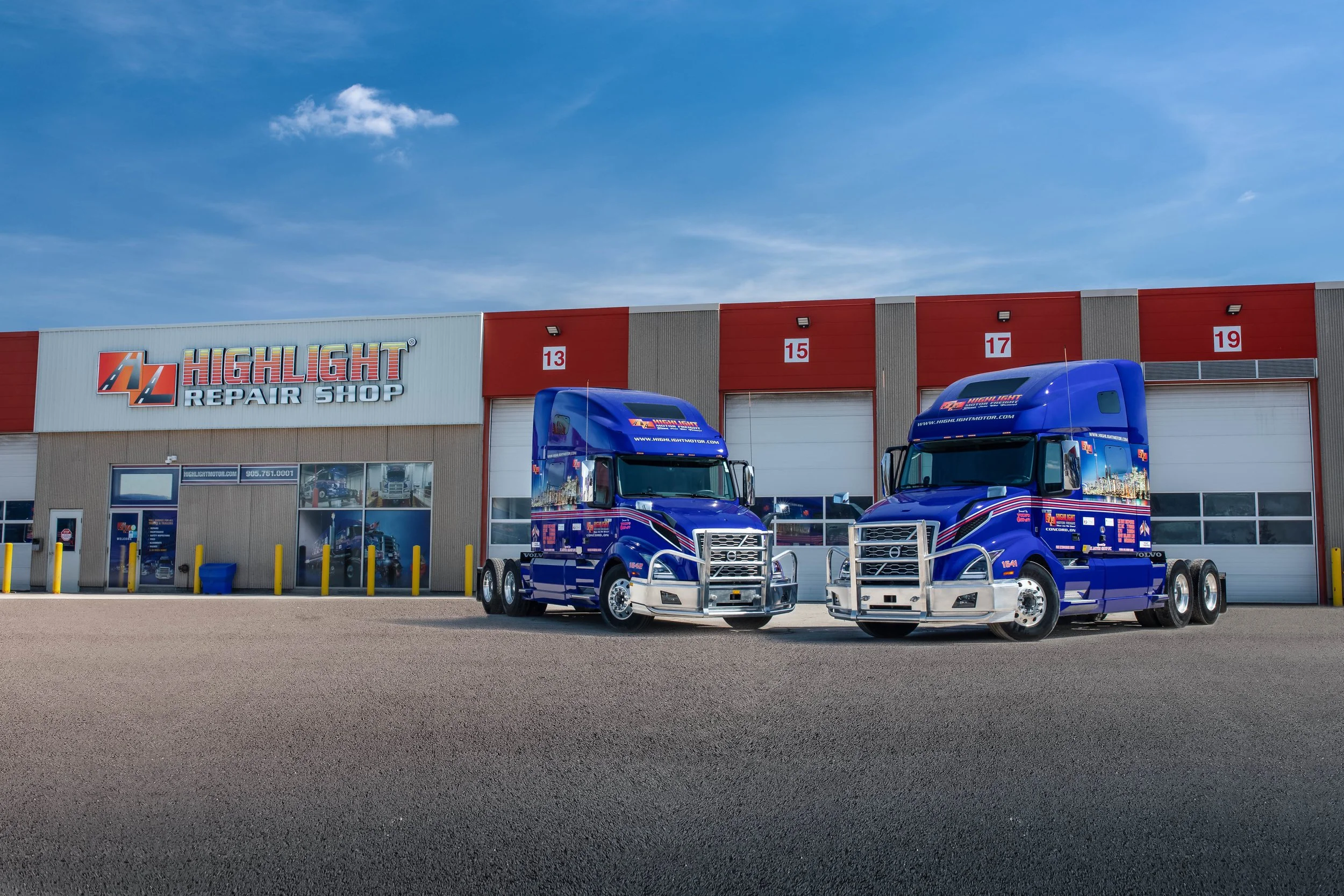 Two blue semi-trucks parked outside 'Highlight Repair Shop' building with numbered garage doors 13, 15, 17, and 19 under a blue sky