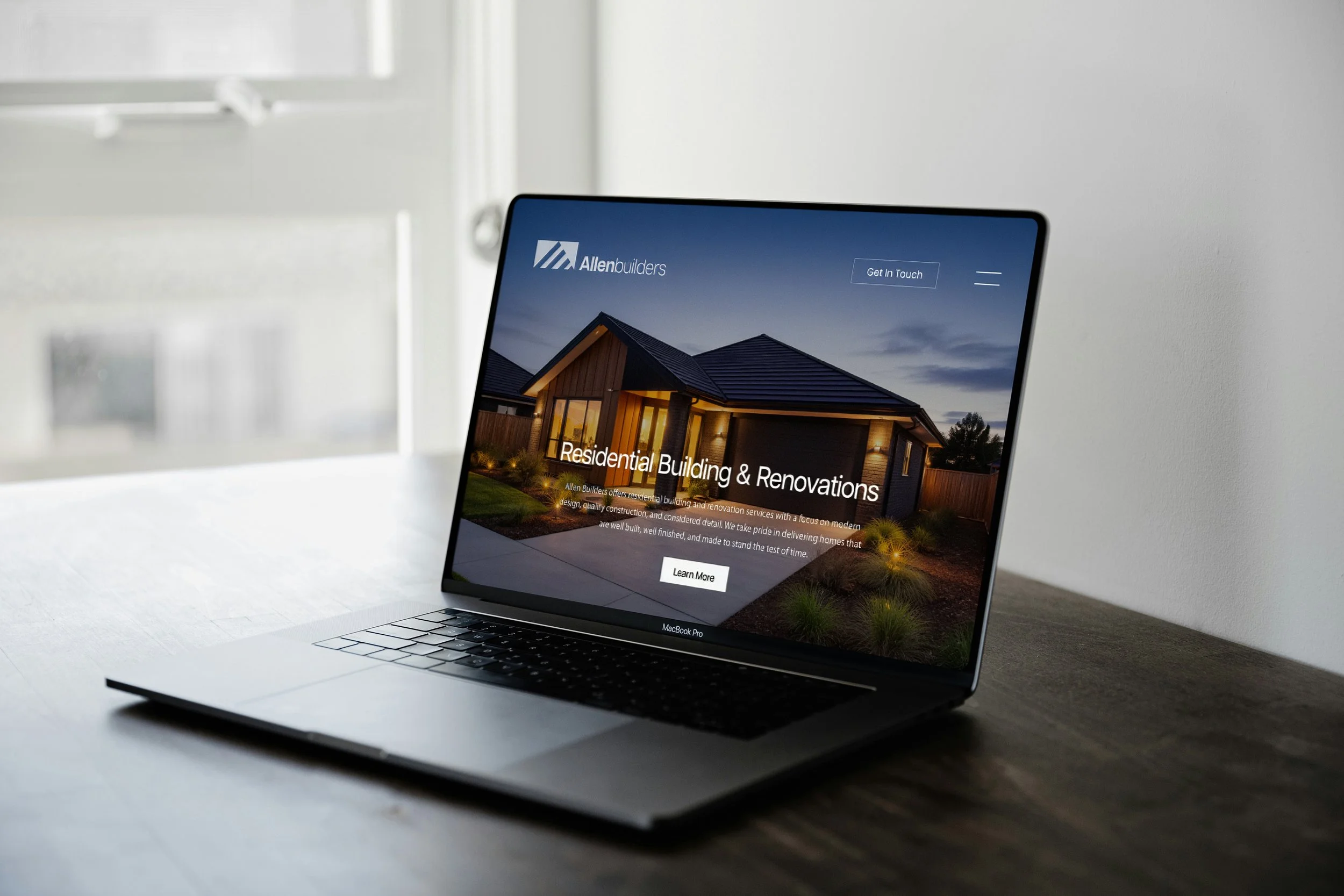 Laptop on a desk displaying a website for residential building and renovations by Allen Builders, showing a house at dusk.