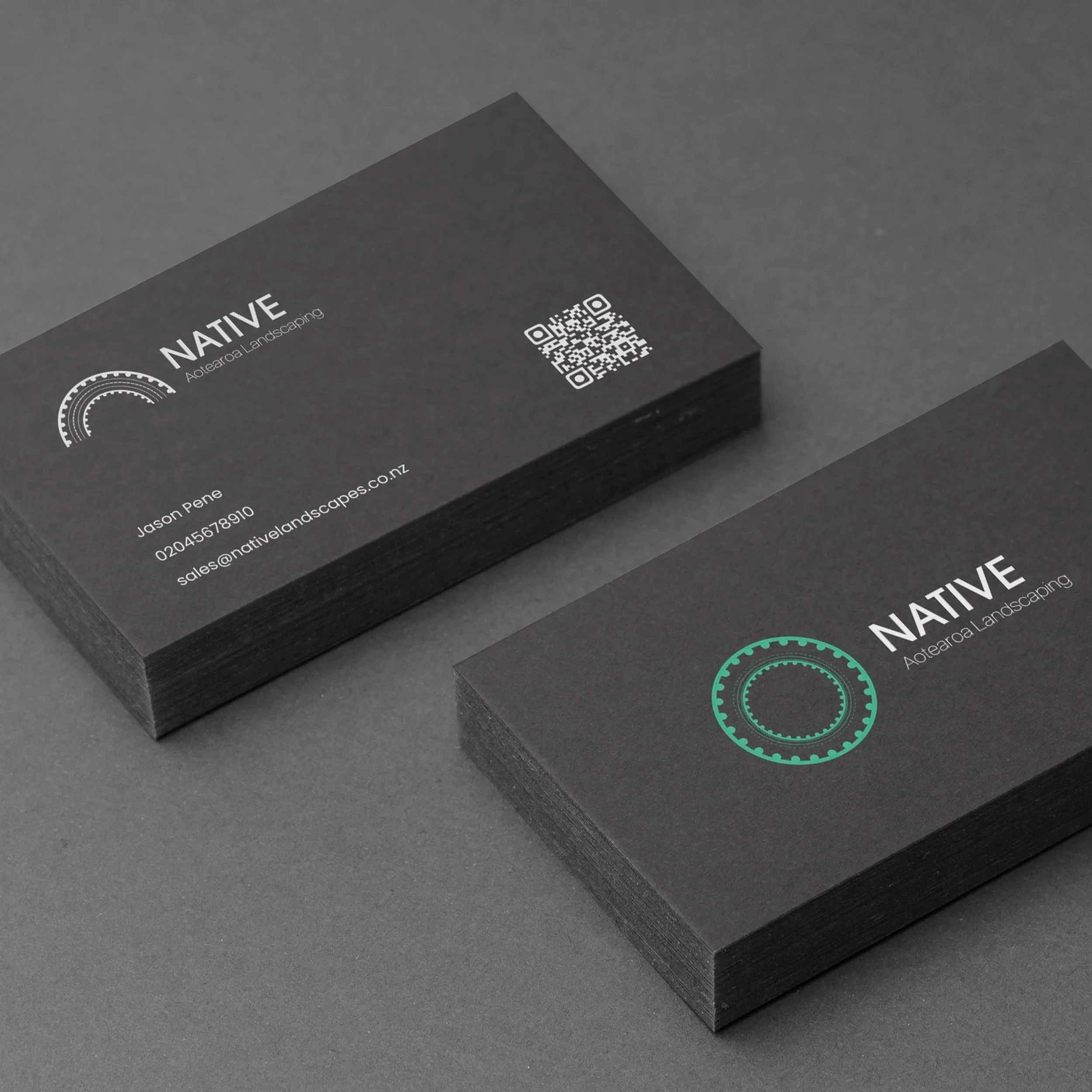 Stack of black business cards for Native Aotearoa Landscaping, featuring a circular logo, contact information, and a QR code, placed on a dark gray surface.