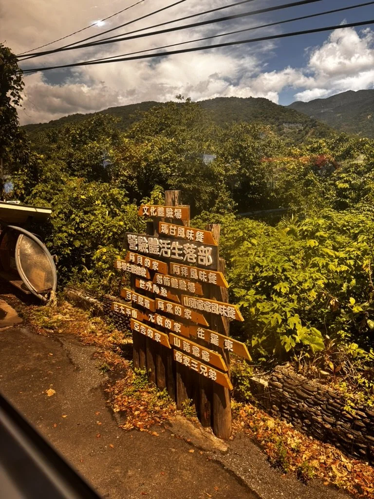 Multiple wooden signposts with Chinese characters pointing in various directions, set in a lush, mountainous landscape during daytime.