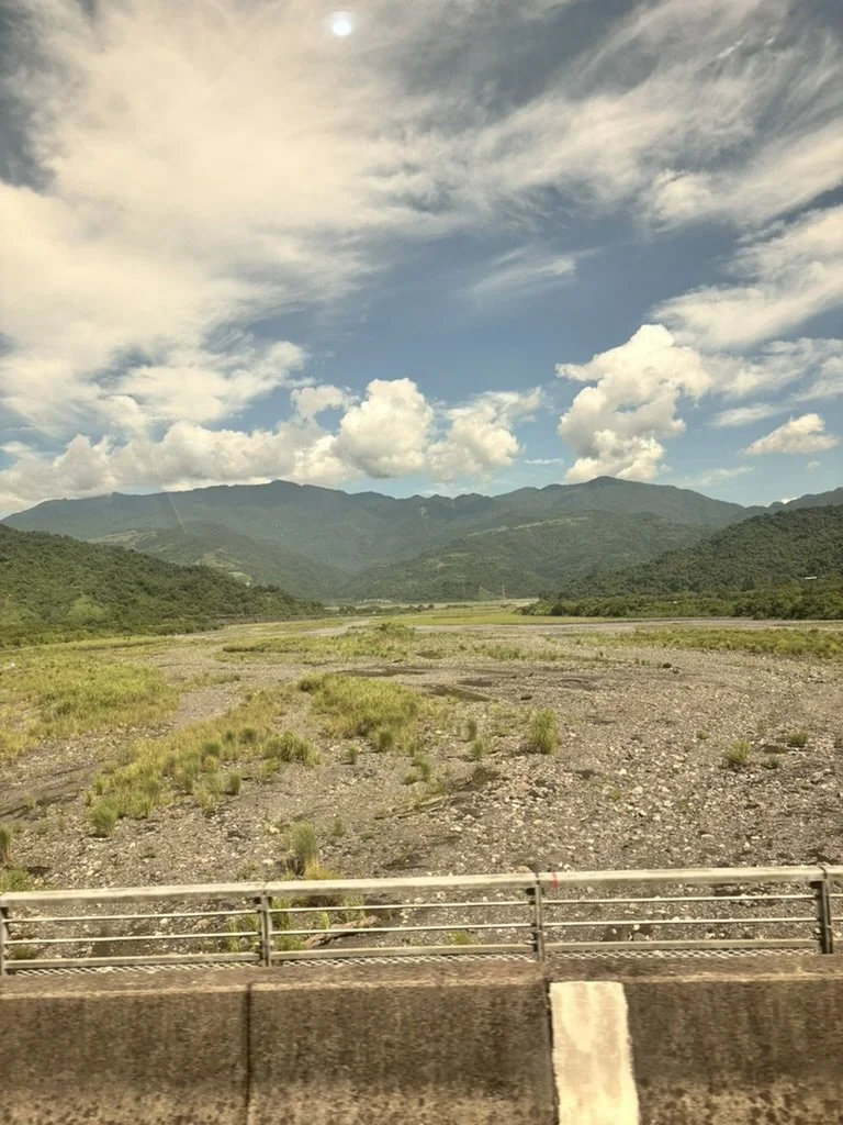 Scenic view of mountains with partly cloudy sky, grassy and rocky terrain in the foreground, and a bridge railing at the bottom.