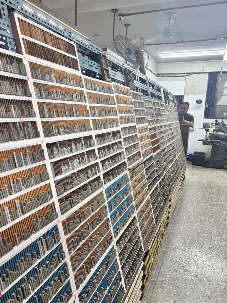 A person inspecting a large display of various metal or plastic rods or pins organized in rows and sections, likely in a manufacturing or industrial setting.