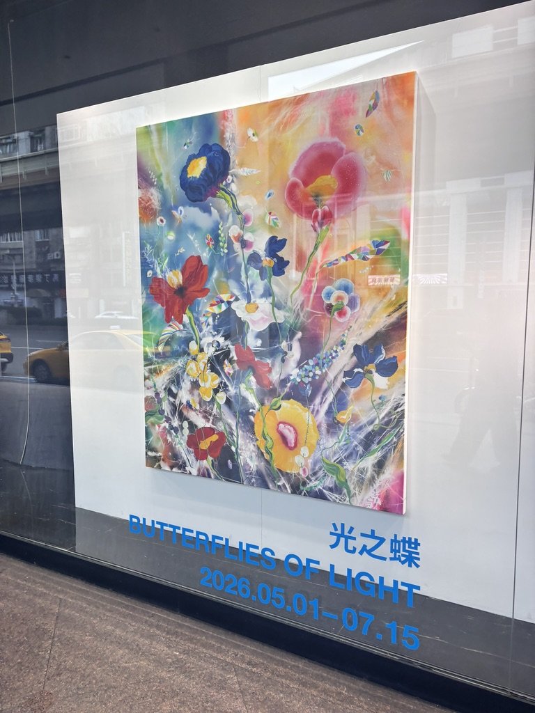 Colorful abstract painting of various flowers with bright, vibrant colors and swirling patterns, titled 'Butterflies of Light', displayed in a glass window, with dates from May 1 to July 15, 2026.