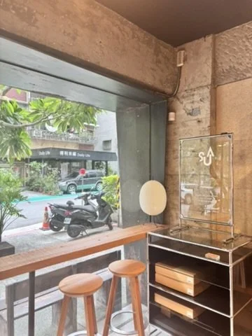 Indoor seating area with two wooden bar stools near a large window overlooking a street with parked motorcycles and trees.
