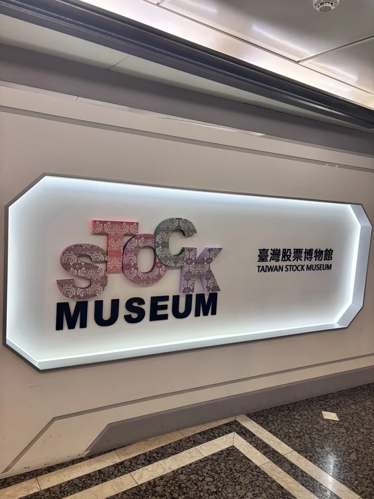 Sign for the Taiwan Stock Museum with decorative letters spelling 'STOCK' and the word 'MUSEUM' in bold letters beneath, mounted on a wall in an indoor setting.