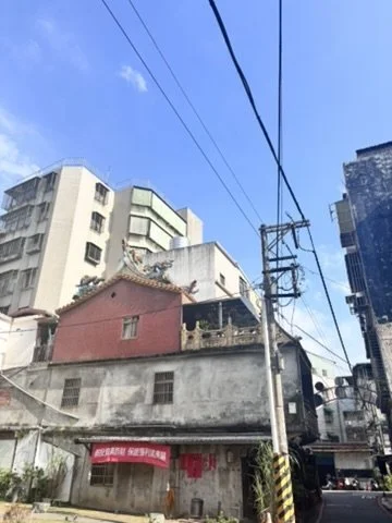 Urban street scene with old and modern buildings under a clear blue sky, power lines overhead, and a narrow street below.