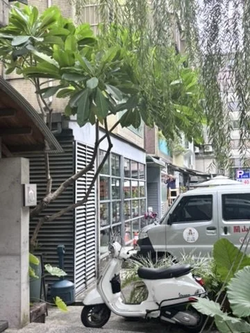 Urban street scene with a small tree, a white scooter, and a parked van with signage in an Asian language.