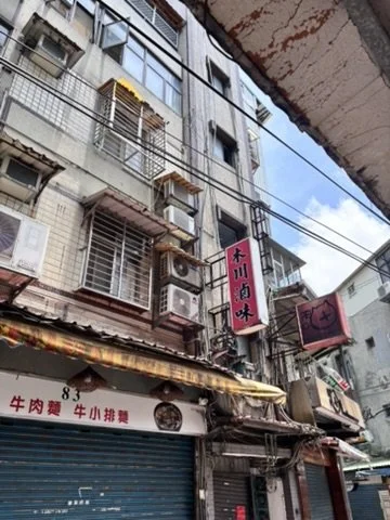 Exterior of a multi-story building with various signs, air conditioning units, and wires in an urban area.
