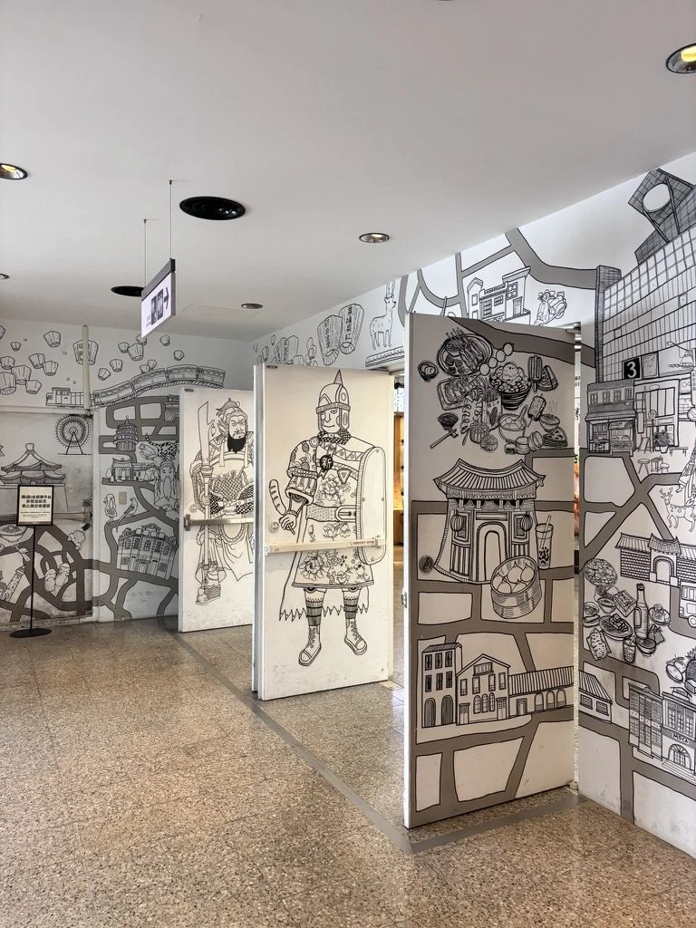 Black outline drawings of various Asian cultural and historical scenes, characters, and architecture on white display panels in an indoor setting.