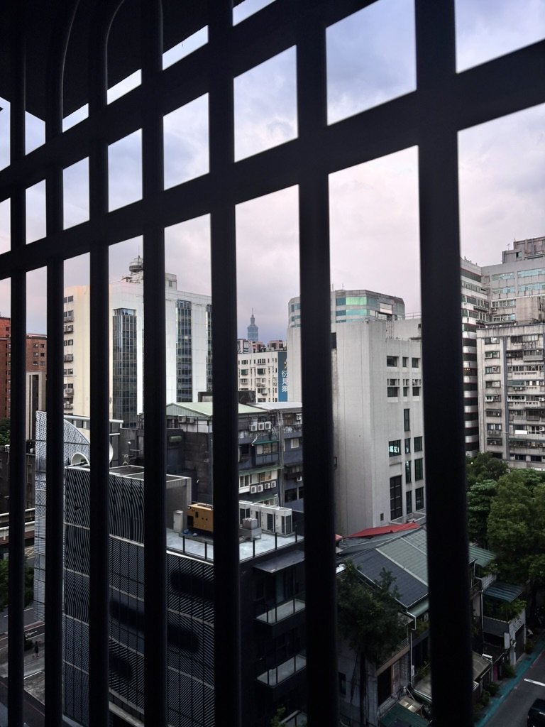 View of city buildings through black metal balcony railing on an overcast day.