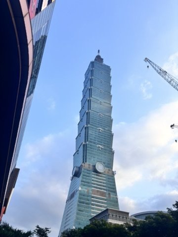 Tall skyscraper with modern glass architecture under a blue sky with some clouds.