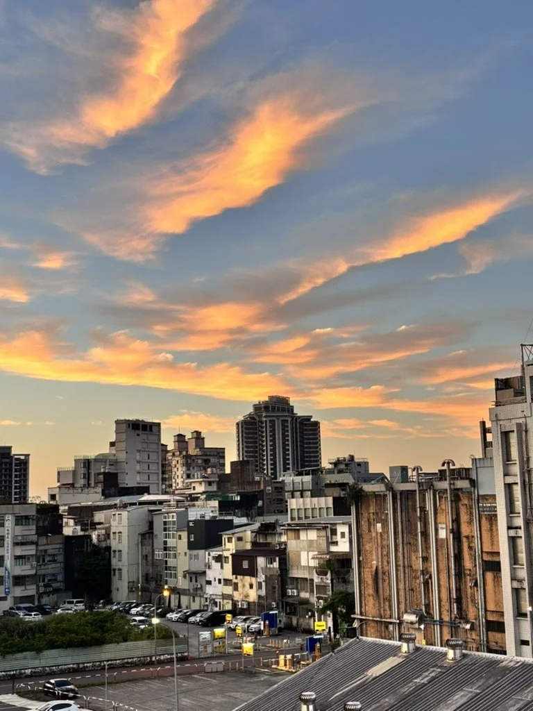 City skyline during sunset with colorful clouds in the sky, high-rise buildings, and a parking lot in the foreground.