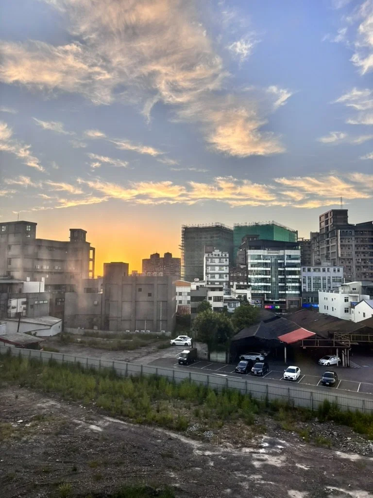 Cityscape at sunset with buildings, clouds, and parked cars.