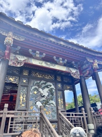 Traditional Asian temple with intricate woodwork and dragon carvings on the doors, under a blue sky with clouds.
