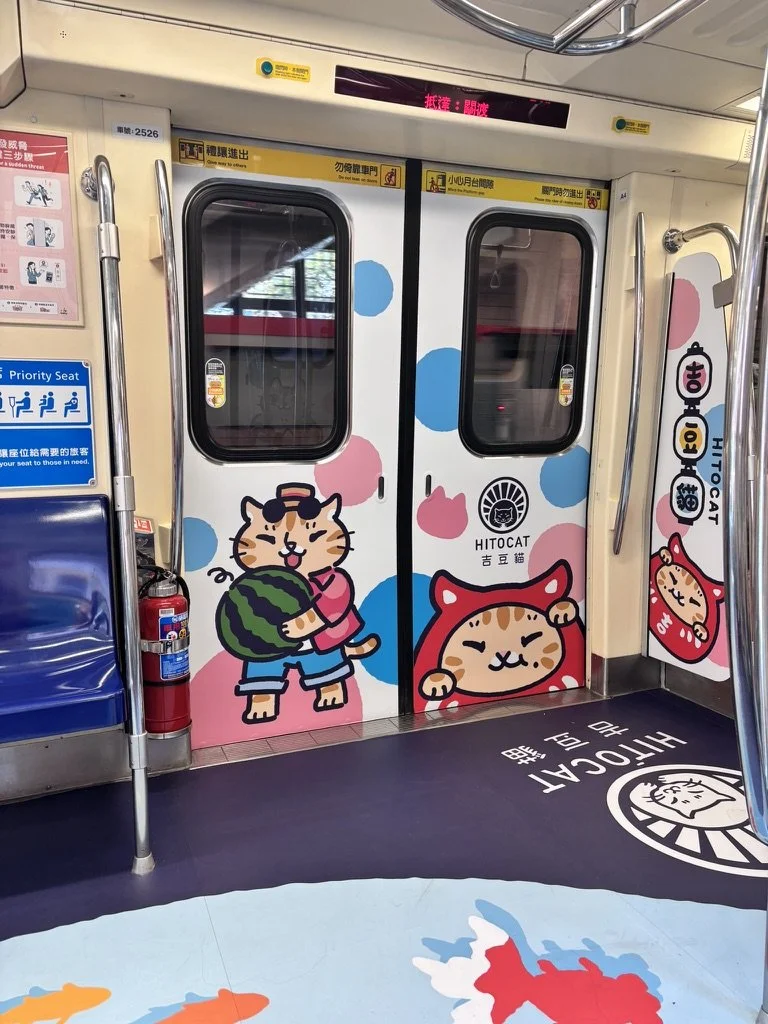 Colorful cartoon cat characters on train doors, including a cat holding a watermelon and another in a red hood, with pink and blue polka dot background decorations.