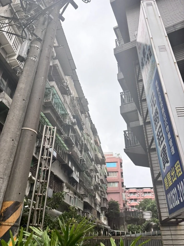 Tall apartment buildings on a city street with balconies, a utility pole, and a sign with Asian characters.