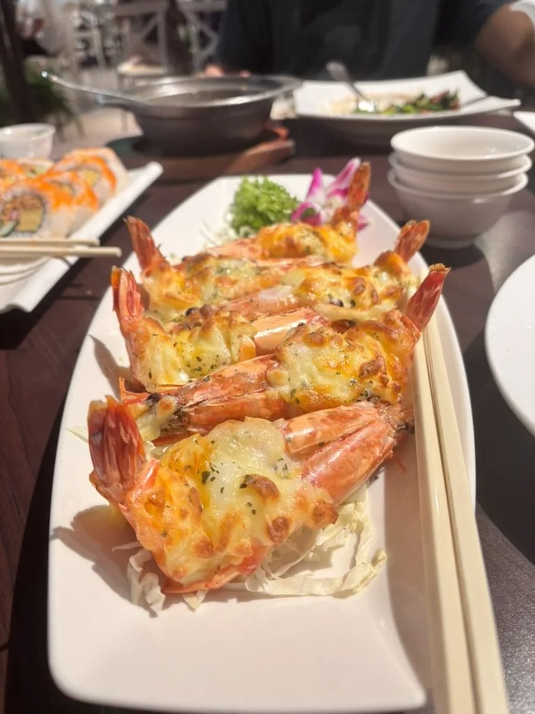 Baked shrimp with melted cheese on a white rectangular plate, garnished with lettuce and pink radish slices in the background.